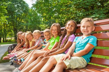Happy children sit on the bench in park