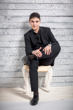 Man In Suit Sitting On Chair With Legs Crossed At Studio