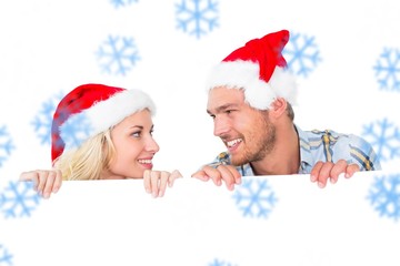 Composite image of festive couple smiling from behind poster