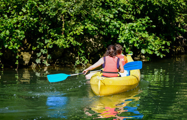 Two kids canoeing in a bautifull lake surrounded by green nature