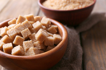 Brown sugar cubes and crystal sugar in bowl on wooden
