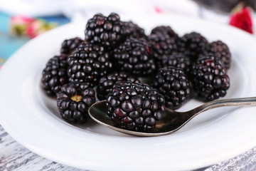 Sweet blackberries on plate, on color wooden background