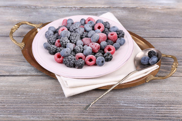 Iced berries on plate, on color wooden background