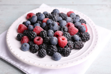 Iced berries on plate, on color wooden background