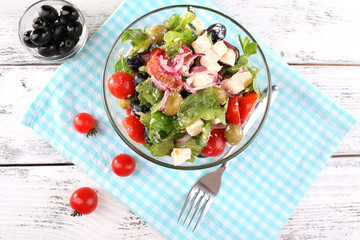 Glass bowl of Greek salad served on napkin on wooden background