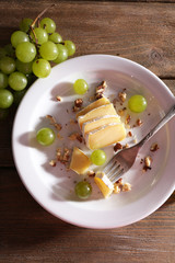 tasty grape and cheese on plate, on wooden table