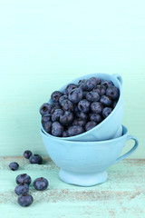 Tasty ripe blueberries in cups, on wooden table
