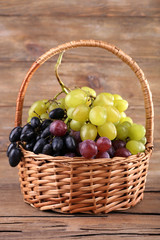 Different kinds of grapes in wicker basket on wooden background