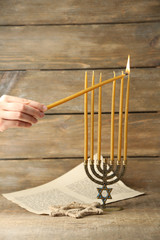 Hand burning candles on Menorah on wooden background