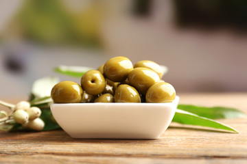 Green olives in bowl with leaves on table on light background