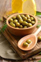 Green olives in bowl with leaves on table close-up