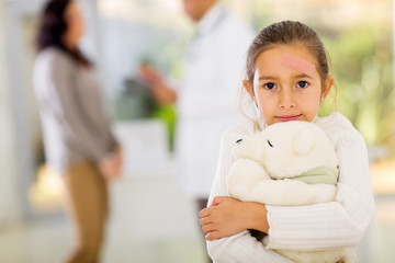 Girl with adhesive bandage on her face holding a teddy bear