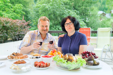 The senior couple drink red wine on terrace in sunny day