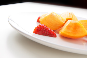 Fresh strawberries and persimmons on white plate.