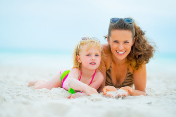 Portrait of smiling mother and baby girl laying on beach
