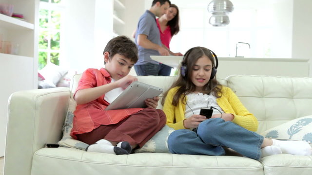 Children Playing With Digital Devices As Parents Make Meal
