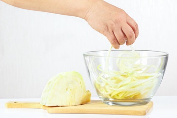 Female hand takes shredded cabbage in a glass bowl