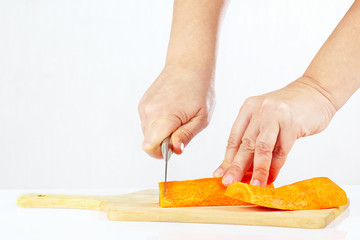 Female hands with a knife chops carrot on a cutting board
