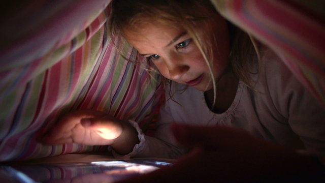 Girl Looking At Digital Tablet In Under Bed Cover At Night