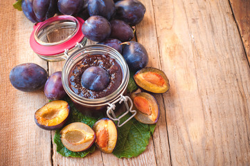 Jar of plum jam surrounded by plums on background wooden rural t