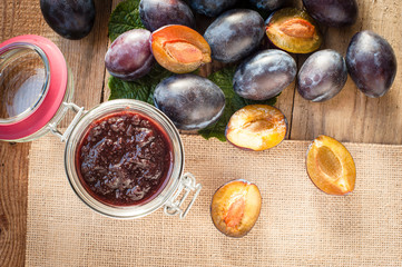 Jar of plum jam surrounded by plums on background wooden rural t