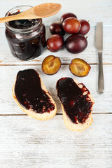 Bread with plum jam and plums on wooden table