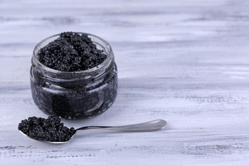 Fototapeta na wymiar Glass jar and spoon of black caviar on grey wooden background