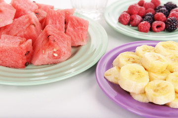 Sliced fruits and berries on plate with glass of water close up