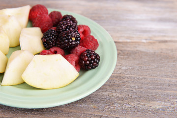Slices of fruits with berries on plate on wooden table