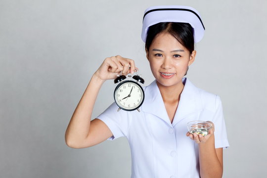 Young Asian nurse with clock and pills on her palm hand