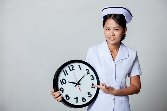 Young Asian nurse point to a clock