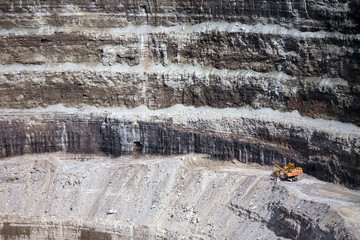 Wall of a modern diamond mine and a big yellow machinery