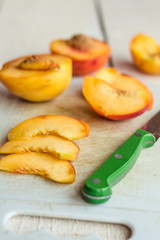 slices of ripe peach on a white board, green knife