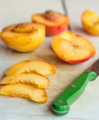 Naklejka na ściany i meble slices of ripe peach on a white board, green knife