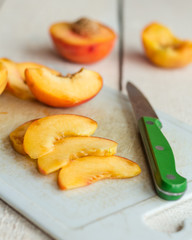 slices of ripe peach on a white board, green knife