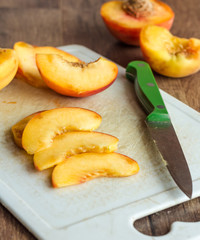 cut slices of ripe peach on a white board, green knife