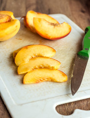 cut slices of ripe peach on a white board, green knife