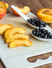 peach slices and blueberries in spoon on a white board