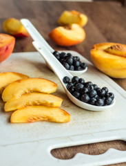 peach slices and blueberries in spoon on a white board