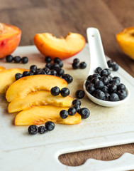peach slices and blueberries in spoon on a white board
