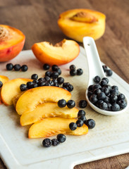 peach slices and blueberries in spoon on a white board