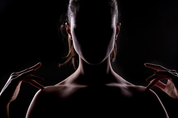 woman with the face in the shadow touches her shoulders