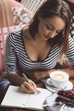 Girl drawing a cup of coffee in the notebook