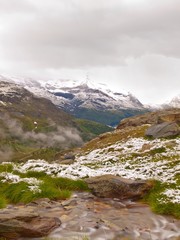 September snow on Alpine meadow, cascade on stream.