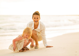 Happy mother and baby girl playing on the beach in the evening