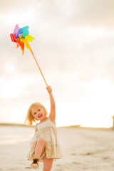 Happy baby girl playing with colorful windmill toy on the beach