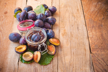 Jar of plum jam surrounded by plums on background wooden rural t