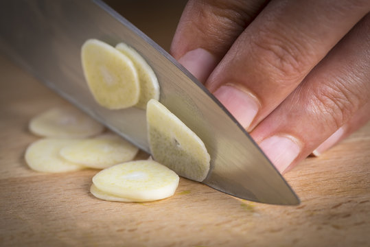 Cocinero cortando ajos laminados con el cuchillo en la cocina