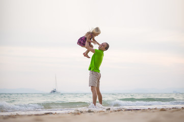 Father lift up daughter on hands on sunset ocean beach with yach