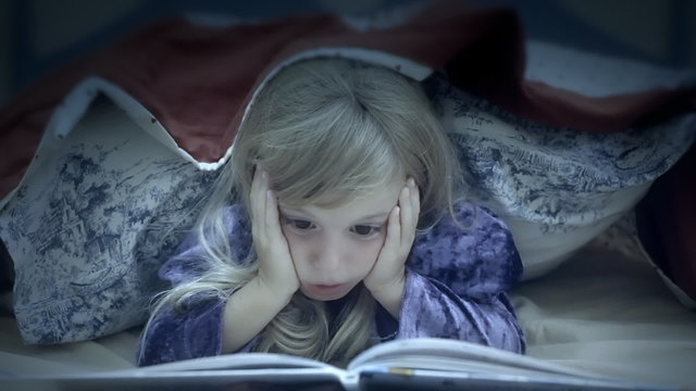 Little girl under bed sheets reading scared